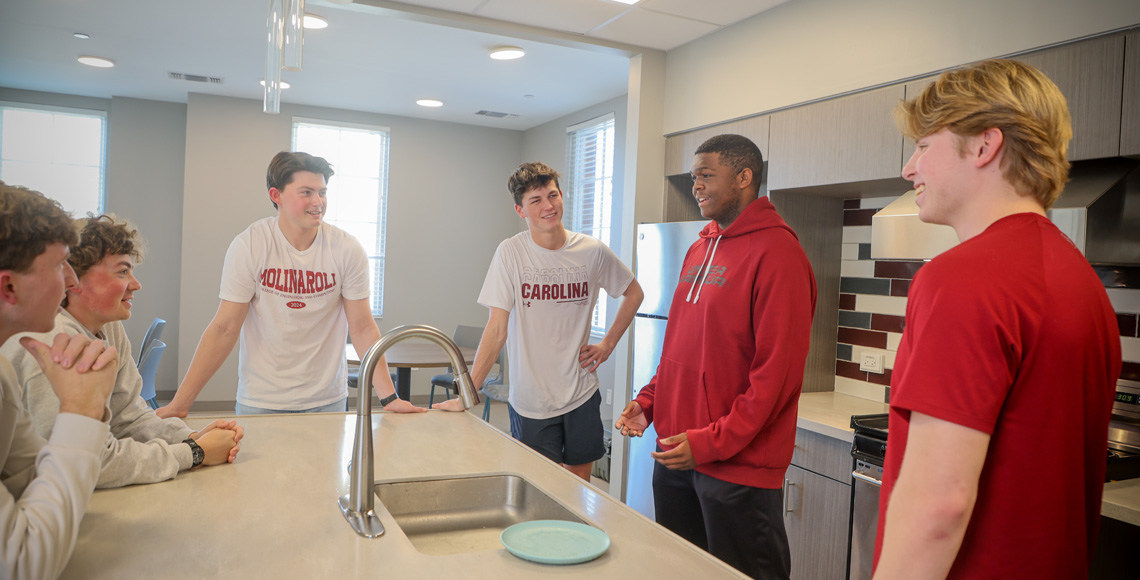 six guys stand around a kitchen island talking in their gamecock gear