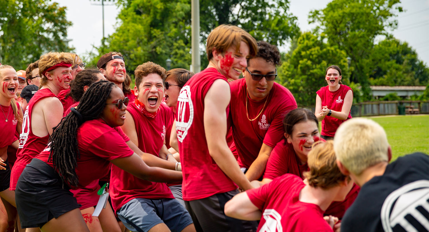 Group of students all wearing garnet tshirts working together pulling on a rope in a huge tug-o-war game. 