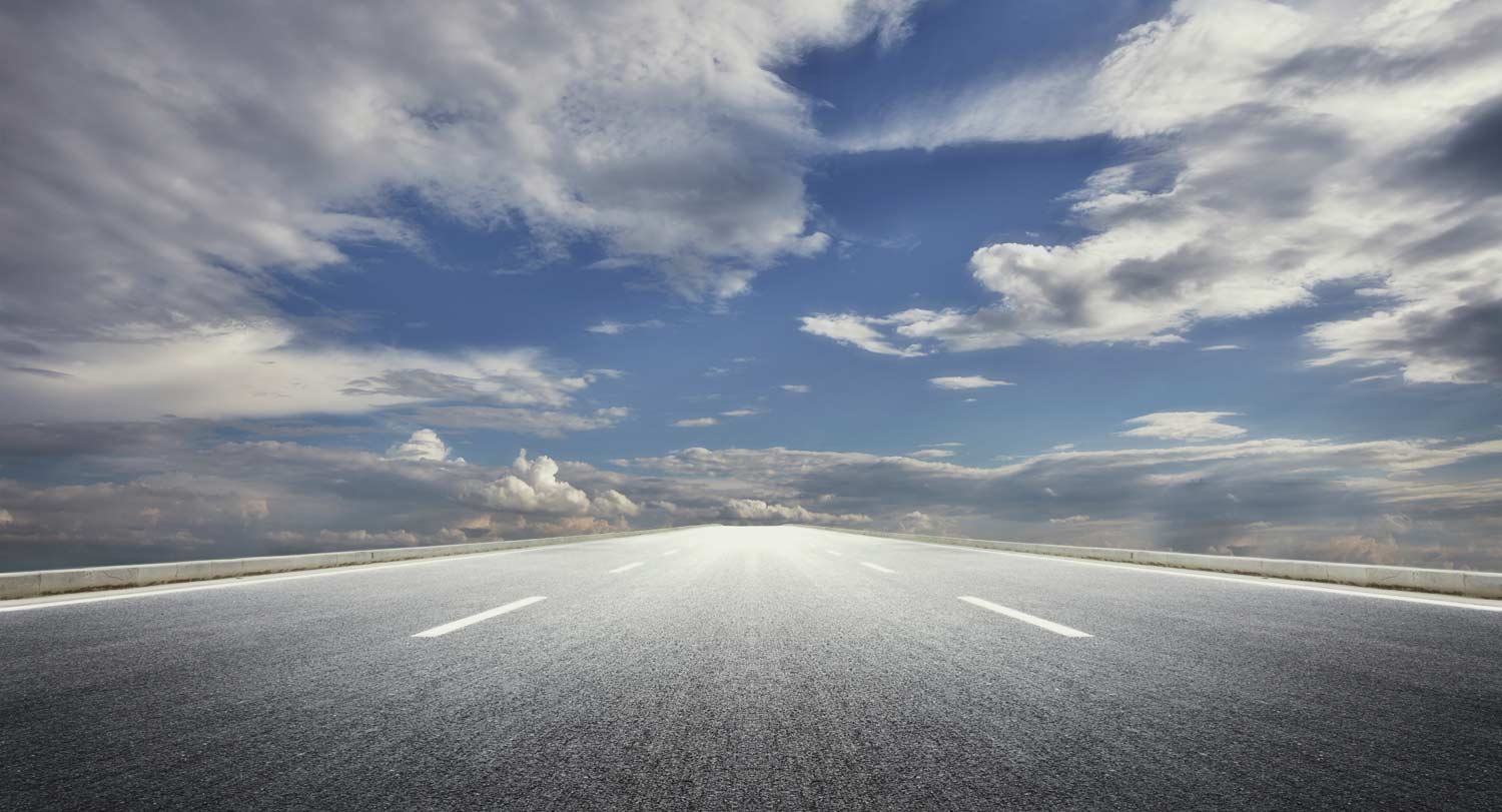 An open road or highway with a blue, cloudy sky.