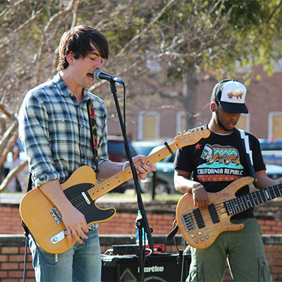 Guy playing a guitar singing into a microphone on an outdoor stage. 