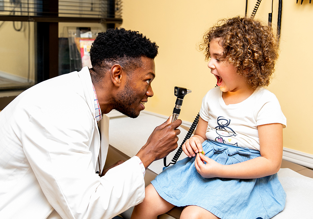 Doctor looking into a child's throat in an exam room.