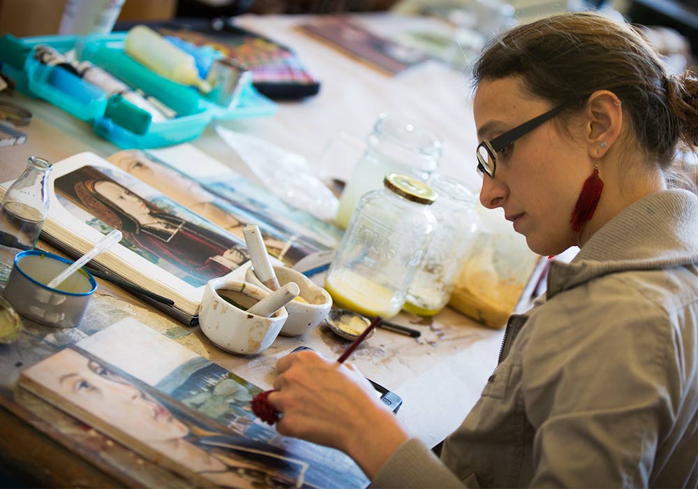 Person painting surrounded by art supplies. 