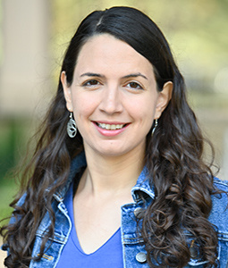 a woman outside smiling with dark  hair and a jean jacket on