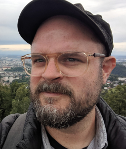 Chaz Evans in glasses and hat outside of a city