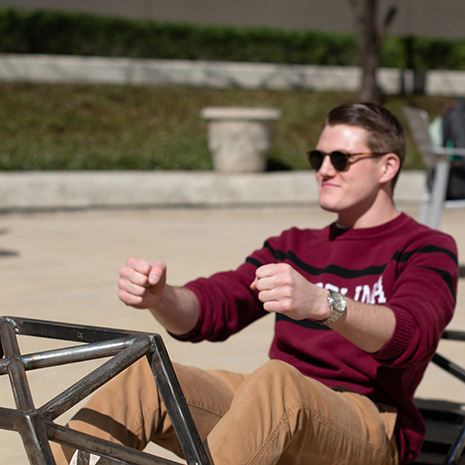 student sits in metal car frame pretending to drive