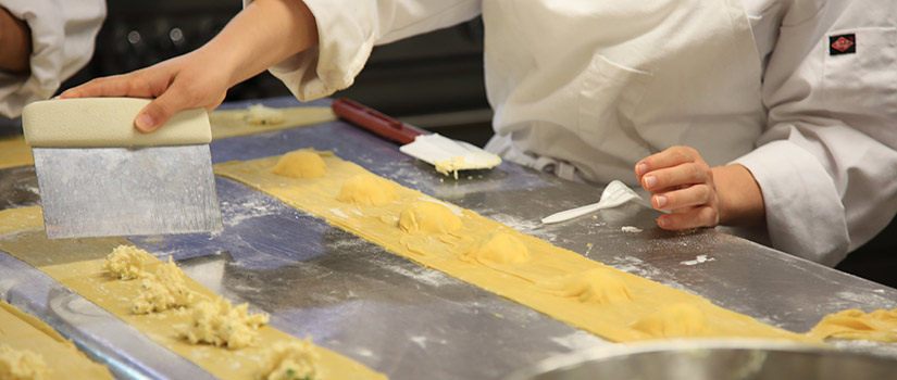 A culinary student learns how to make fresh pasta and from that create ravioli. Here her hands are shown cutting the pasta to ravioli size.