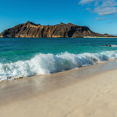 Landscape of strong waves by the beach in Stephens Bay with Witch Hill in the background, San Cristobal, Galapagos Islands, Ecuador.