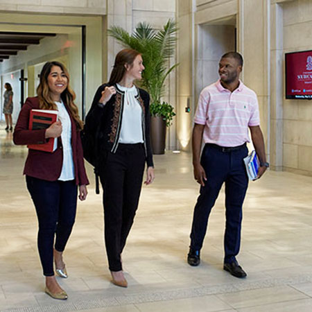 three students walking side by side and talking in the school of law lobby.