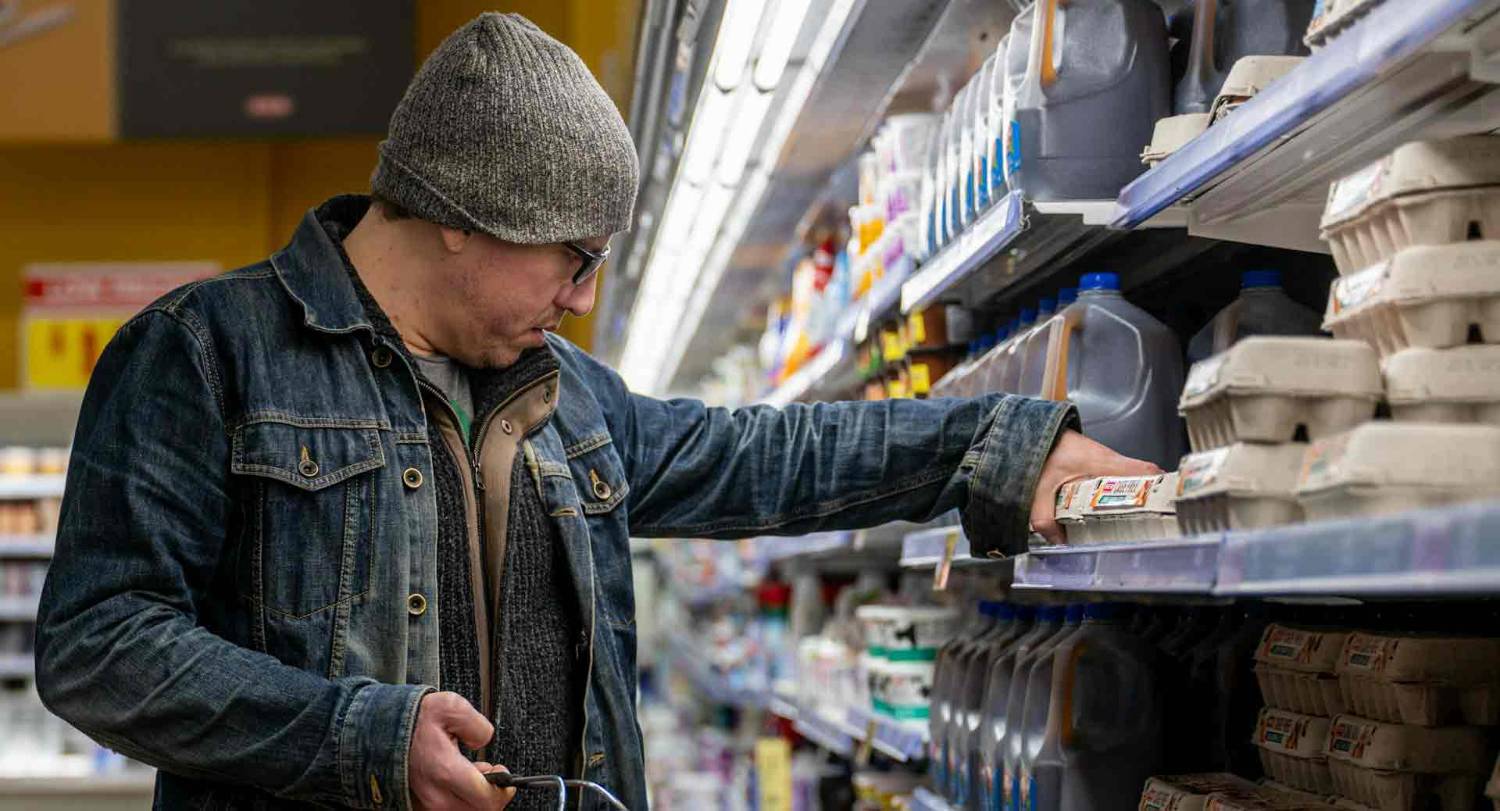 A supermarket customer reaches for a carton of eggs.