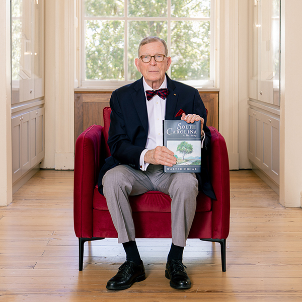 Walter Edgar sits in a red chair and holds his book 'South Carolina A History.'
