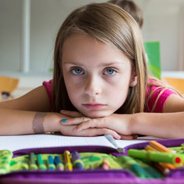 girl with chin on arms with notebook and crayons