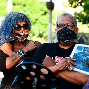 A woman and a man make the Wakanda gesture. Man holds a photo of actor Chadwick Boseman.