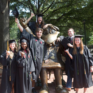 students in graduation robes surround the cocky statue on campus