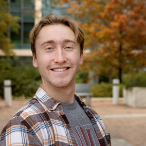 man stands outside with trees and a building in the background